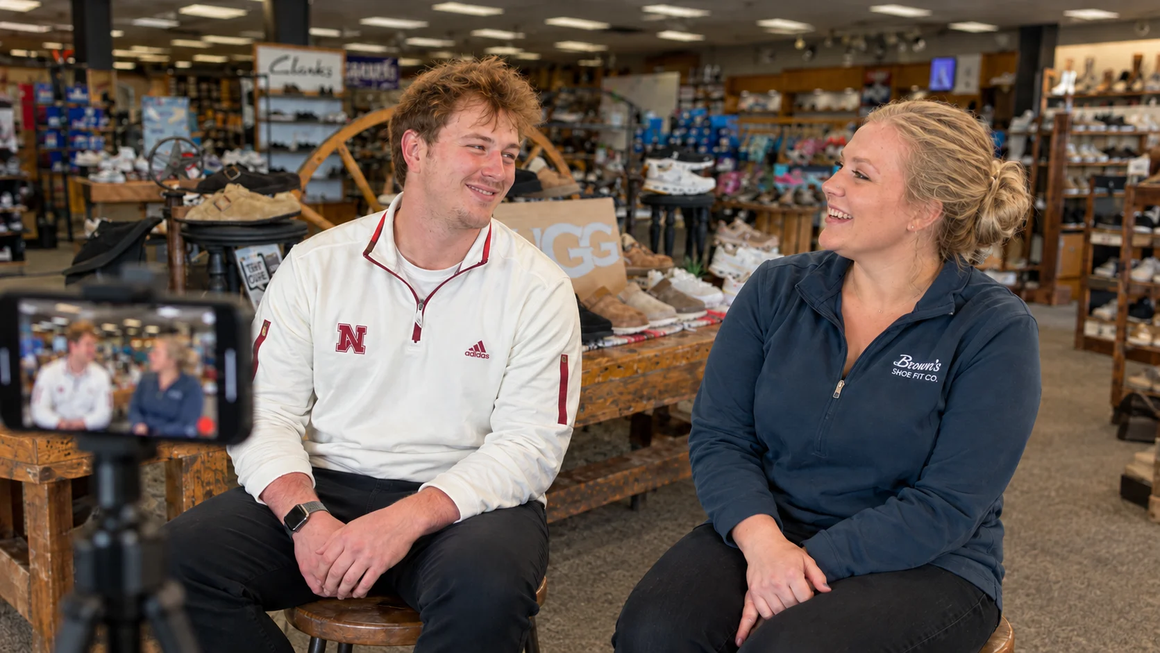 Avery and Callen of Brown's Shoe Fit Co. chatting beside a UGG and Birkenstock display inside a Brown's store while a smartphone records them